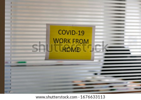Worker puts a sign showing 'COVID-19: Work from Home'. Business office is closed during the pandemic control for Coronavirus or COVID-19 prevention. Worker takes 14-day self quarantine away from desk.