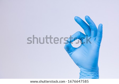 Ok sign is showed by left man hand in a blue medical glove on a white background. Okay