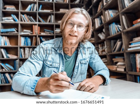 Male online tutor english teacher job applicant looking at camera teaching student web class online lesson training do videocall make note communicate at distant job interview in library, webcam view. Royalty-Free Stock Photo #1676651491