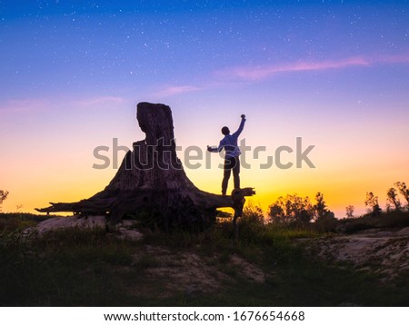 Silhouette man stane alone on tree stump at night sky background with  stars on the sky.