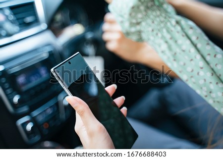 Woman hand holding smartphone in the car in passenger seat.