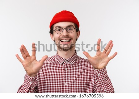 Close-up portrait funny hipster guy in red beanie and glasses make spok gesture showing fingers and smiling, discuss favorite tv series with friends geeks, standing white background upbeat