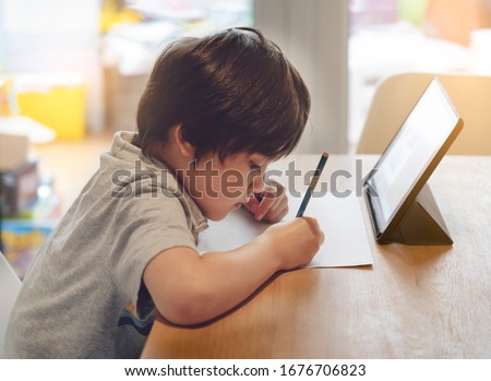 Child kid using tablet for homework at home,Student study research information online internet,Education Ai Technology,Asian Young Boy Concentration read and writing on notepad book,Preschool lesson
