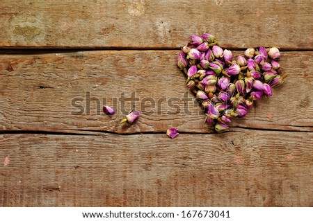 Dry roses in a shape of heart on wooden background 