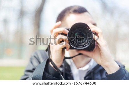 A black DSLR camera was held by an unknown man who posed shooting it straight into the camera. Royalty-Free Stock Photo #1676744638