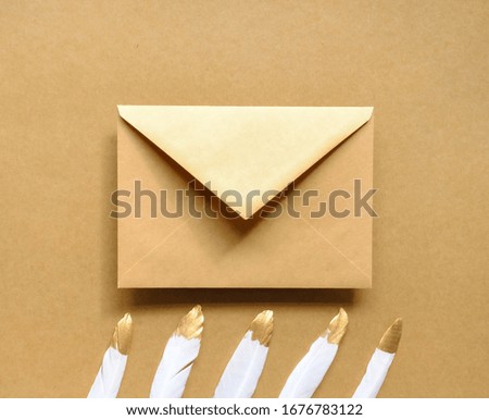 Kraft paper envelope and white golden feathers on brown background. Festive Easter minimal concept. 