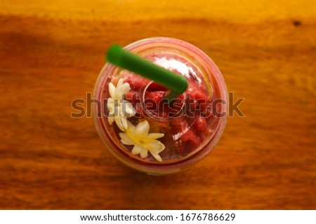 Close-up picture of fruit smoothies in a clear plastic glass with green tubes on top, decorated with white jasmine on a wooden table It is a refreshing and cool drink in summer of Thailand.