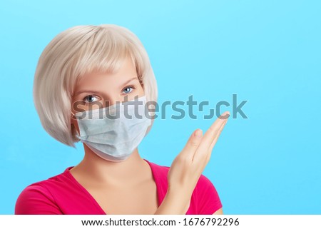 Young beautiful girl with blond hair in a medical protective mask points with her hand to a blank space for text. Prevention, virus protection concept