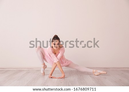 Beautiful young ballerina near light wall