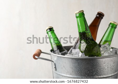 Metal bucket with bottles of beer and ice cubes on grey background