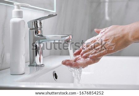 Young woman washing cleansing soapy hands in bathroom to prevent coronavirus infection, cleaning skin care in foam,rubbing hands rinsing with running water. Covid 19 protection concept. Close up view.