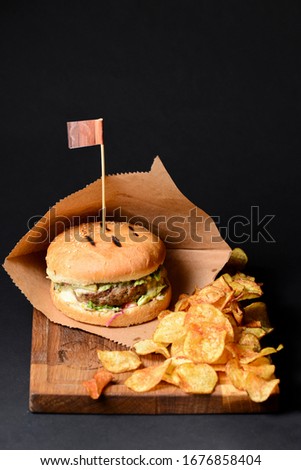 Hamburger with chips served on a wooden cutting board on a black background. American cuisine, food photography.