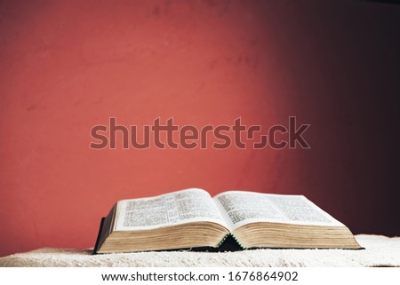 Open Holy Bible on a table. Beautiful red wall background.