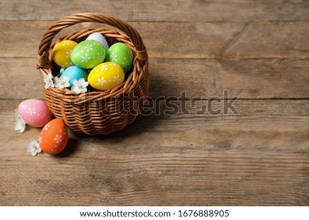 Colorful Easter eggs in basket and flowers on wooden background. Space for text