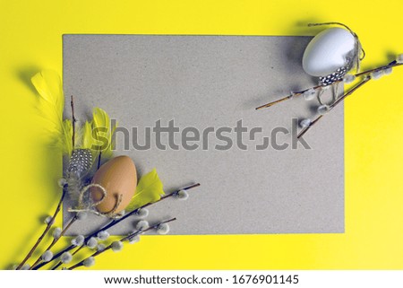 Easter frame from a sheet of gray paper on a yellow background next to Easter eggs, pussy-willow twigs, quail eggs, yellow feathers. Copy space, top view. Creative easter concept