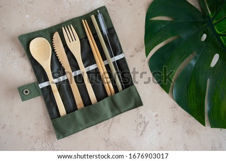 Eco friendly cutlery set, knife fork spoon, chopsticks  and bamboo straw with storage Bag on beige natural background with green monstera leaf . Zero Waste travel utensils Royalty-Free Stock Photo #1676903017