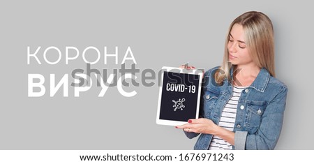 Young woman shows tablet screen with COVID-19 text on it. Text on the background written in Russian 'CORONA VIRUS'