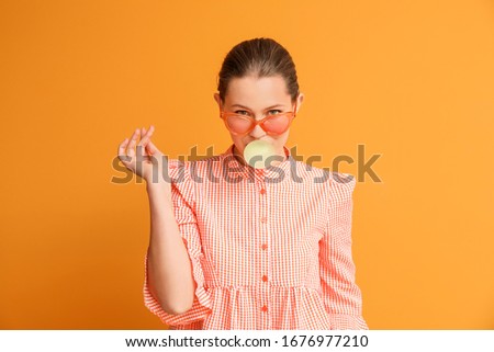 Beautiful young woman with chewing gum on color background