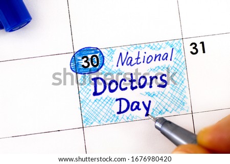 Woman fingers with pen writing reminder National Doctors Day in calendar. March 30.  Royalty-Free Stock Photo #1676980420
