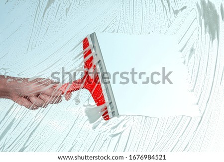 Woman cleaning window with squeegee on spring day, closeup
