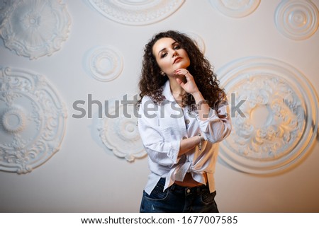 Beautiful young girl model with curls posing. She is wearing a white shirt and jeans.