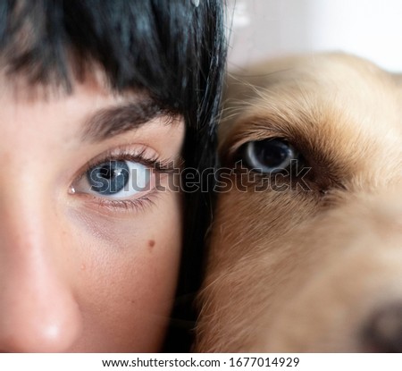 closeup of two eyes. A blue eye of a girl with black hair and a blue eye of a dog