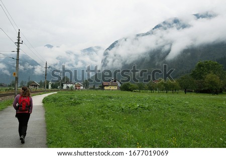 Hiking in Europe.  Athletic and active young woman with a backpack walks along the road towards the mountains covered in fog.  Austrian Alps.  Autumn landscape in the mountains.  Leisure. Lifestyle