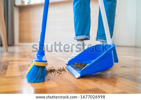 Portrait of young latin man sweeping wooden floor with broom at home. Cleaning, housework and housekeeping concept. Royalty-Free Stock Photo #1677026998