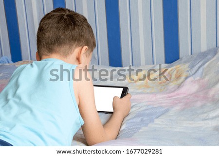 The child uses his the tablet while lying on the bed.