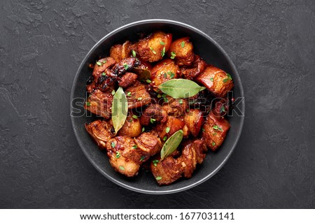 Adobo Pork in black bowl at dark slate background. Pork Adobo or Adobong Baboy is filipino cuisine dish with braised pork belly, bay leaves, soy sauce, vinegar and spices. Filipino food. Top view Royalty-Free Stock Photo #1677031141