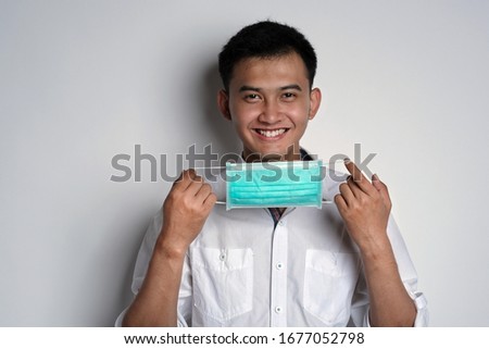 Portrait of young asian man holding a mask while smiling to the camera against white background. Prevention of the spread of corona virus photography concept. Novel Coronavirus (COVID-19)