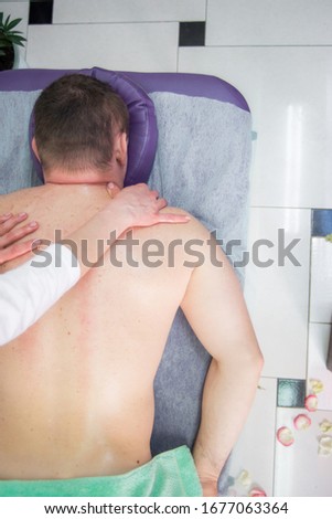 Female massage therapist makes a healing back massage to a man in the massage parlor of a spa salon