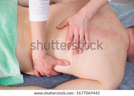 Female massage therapist makes a healing back massage to a man in the massage parlor of a spa salon