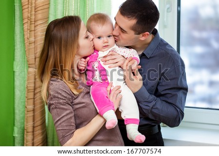 Father and mother are kissing their daughter