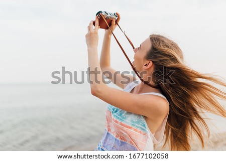 Close- up portrait of a beautiful woman with a retro camera, having fun on the beach, wearing sunglasses.