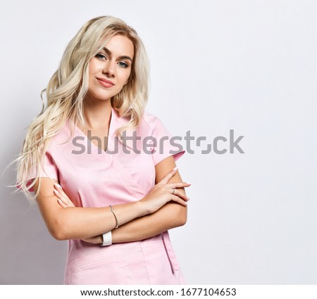 Blond girl in a pink medical suit, smart watch, jewelry posing isolated on white. She smiles, arms crossed over her chest. Medical staff, beautician. Copy space for advertisement. close Royalty-Free Stock Photo #1677104653