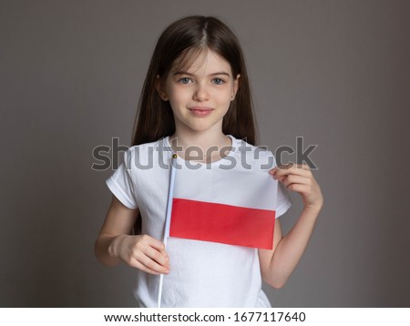 Little / young girl with long hair in a white T-shirt holds the Polish flag. Language school concept. Learning Polish. Immigration to Poland Royalty-Free Stock Photo #1677117640