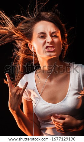Beautiful Woman Listening Music. Attractive smiling happy woman dancing and listening to music in headphone on dark studio background, wearing white shirt. Flying hair and having fun.