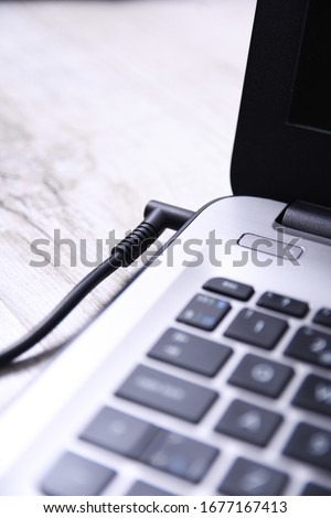 Laptop, computer is charging from a 220-volt outlet on a desk near the wall. Energy, accumulation