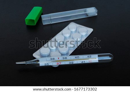 Medical thermometer and pills on a black background