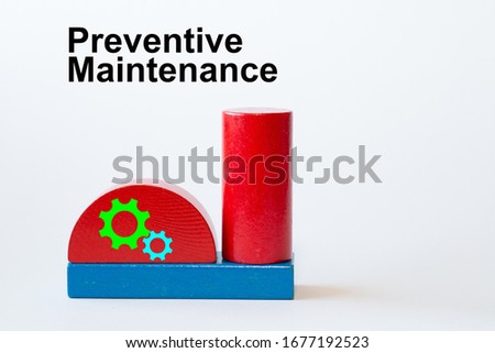 Silhouette of a factory building with chimney made of toy blocks and gear wheel  symbols on the blocks. The heading is against a white background: Preventive Maintenance