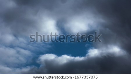 Detail of the sky on a rainy day. Dramatic clouds ranging from dark grey to white. In the middle of an open, you can see the blue sky, wrapped in a tear of light. clouds