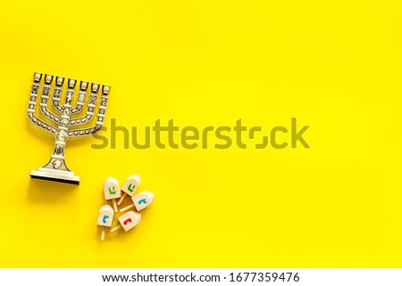 Jewish holiday Hanukkah with menorah - traditional Candelabra - and wooden dreidels spinning top. Yellow background, top view, copy space