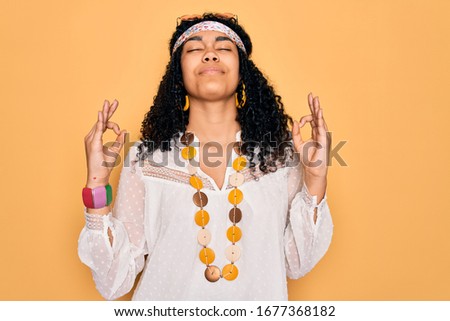 Young african american curly hippie woman wearing sunglasses and vintage accessories relax and smiling with eyes closed doing meditation gesture with fingers. Yoga concept.