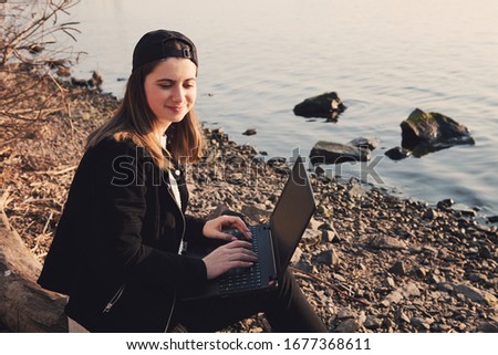 Young female student enjoying work on laptop, doing homework, watching online webinar, listening audio course, writing emails, distantly working with wifi. Concept Distance work, education outdoors