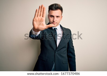 Young handsome business man wearing elegant suit and tie over isolated background doing stop sing with palm of the hand. Warning expression with negative and serious gesture on the face.