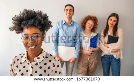 Portrait of a young businesswoman standing in an office with her colleagues in the background. Face of beautiful happy woman looking at the camera on the background of business people