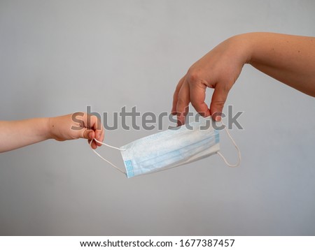 female hand holds out blue surgical mask with rubber ear straps to child. Typical three-layer surgical mask for covering the mouth and nose. (Clipping path). Corona virus protection concept, kid hand
