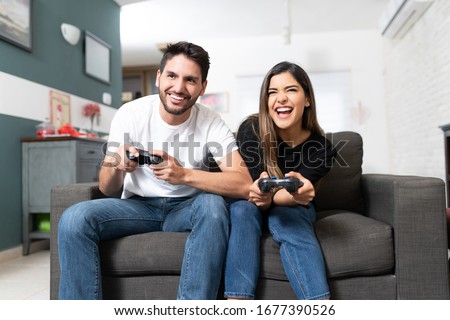 Happy Latin man and woman playing video game while sitting on sofa at home