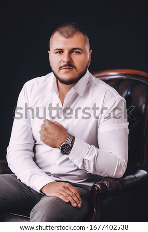 Stock Photo - Confident young man posing at camera in suit. Desaturated portrait over black studio background.

